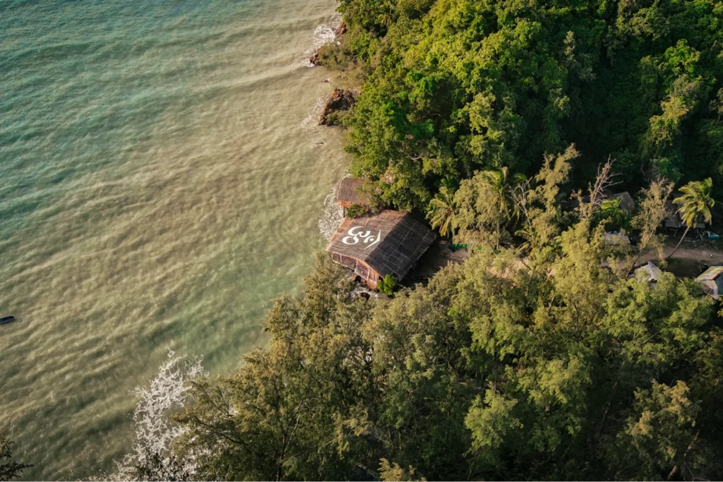 Aerial view of a tropical beachfront yoga training venue surrounded by lush forest in Koh Phangan, Thailand