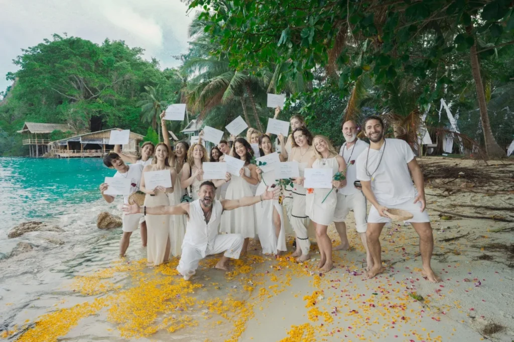 Yoga teacher training graduates celebrating with certificates on a beach in Thailand