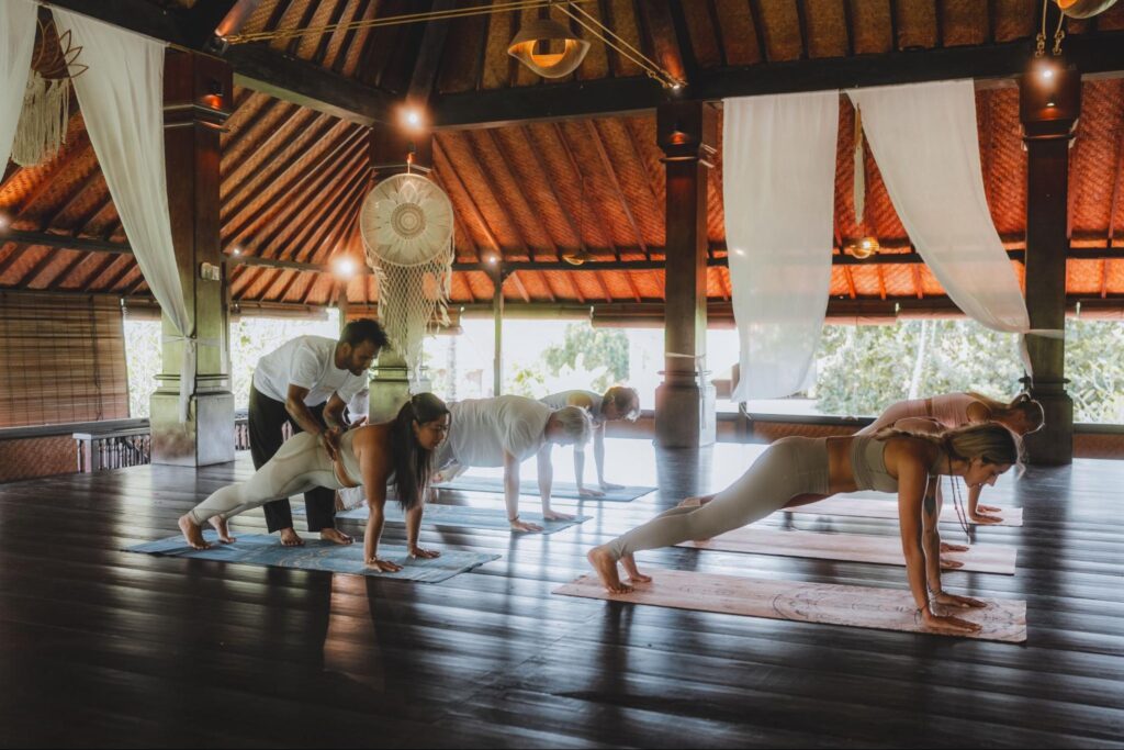 Yoga teacher assisting students during a 200-hour Yoga Teacher Training class at House of Om Bali in an open-air yoga shala.