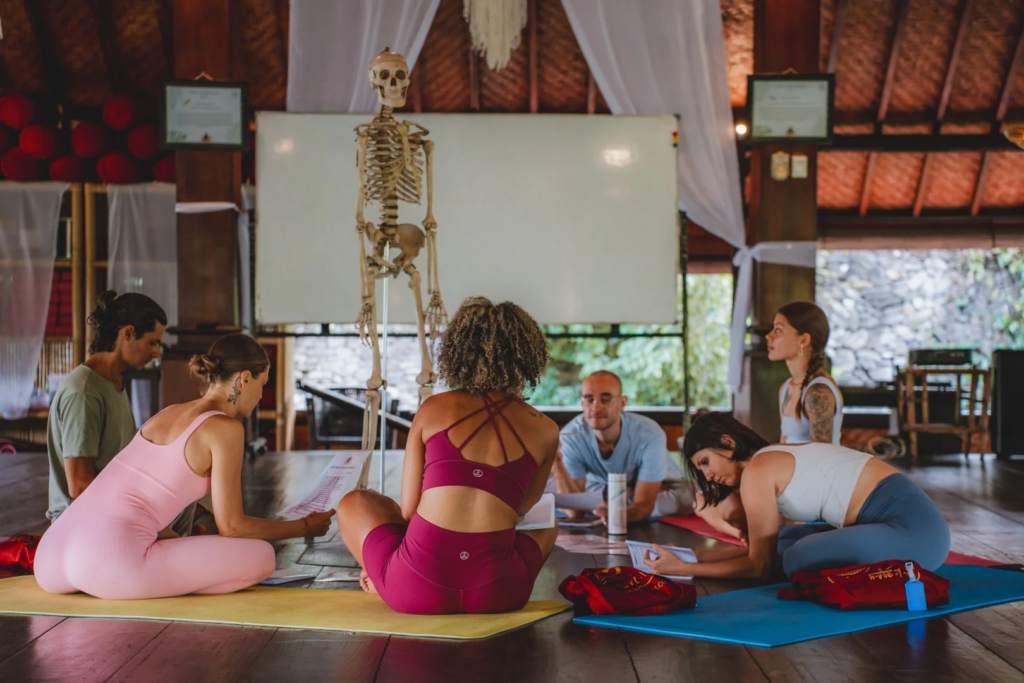 Students learning yoga anatomy with a skeleton model during a Yoga Alliance-certified teacher training course at House of Om Bali.