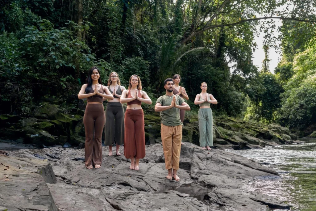 House of Om Yoga Teacher Training students practicing yoga in nature beside a tropical river in Bali.