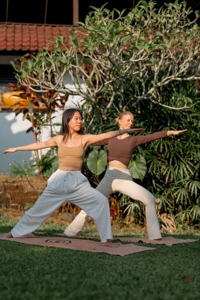 Students practicing Warrior II pose outdoors during a House of Om Yoga Teacher Training in Bali.