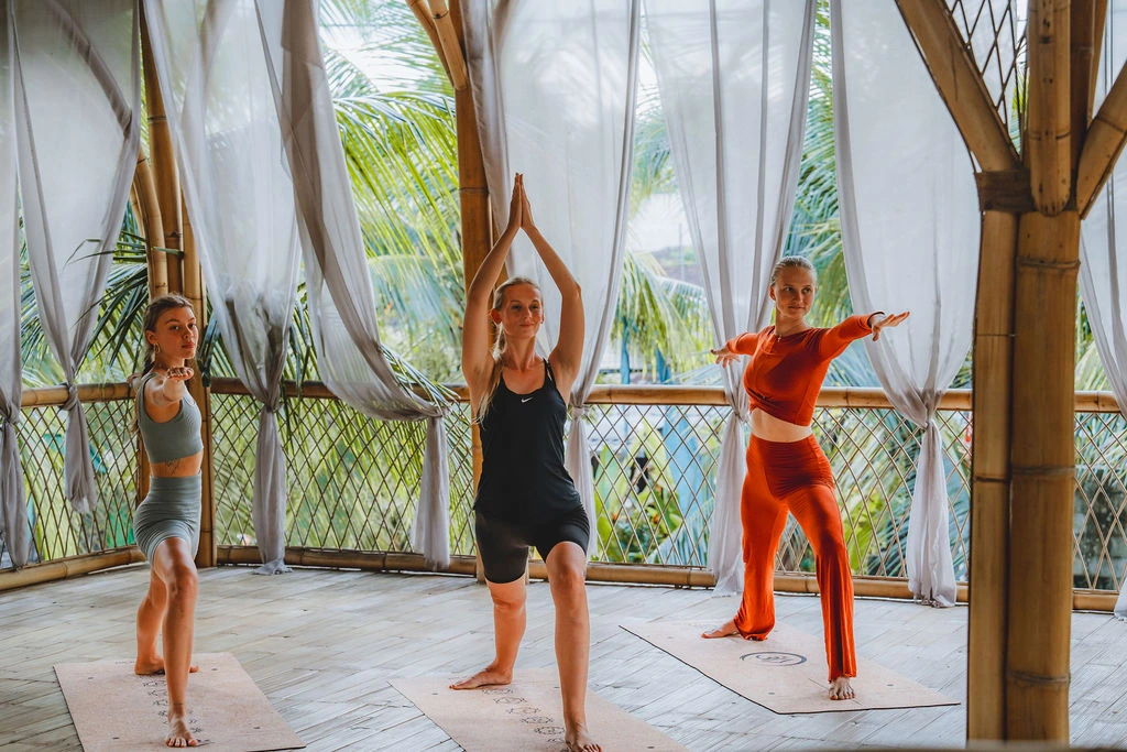 Yoga students practicing standing poses inside a bamboo yoga shala during teacher training