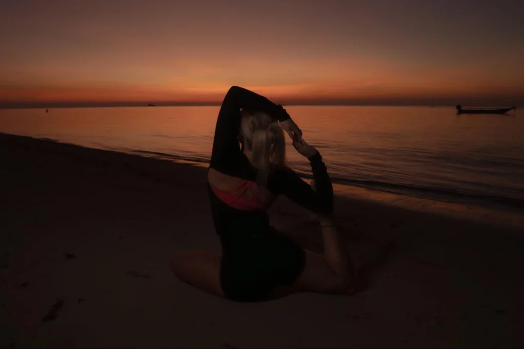 Woman practicing yoga on the beach at sunset during yoga teacher training in Thailand