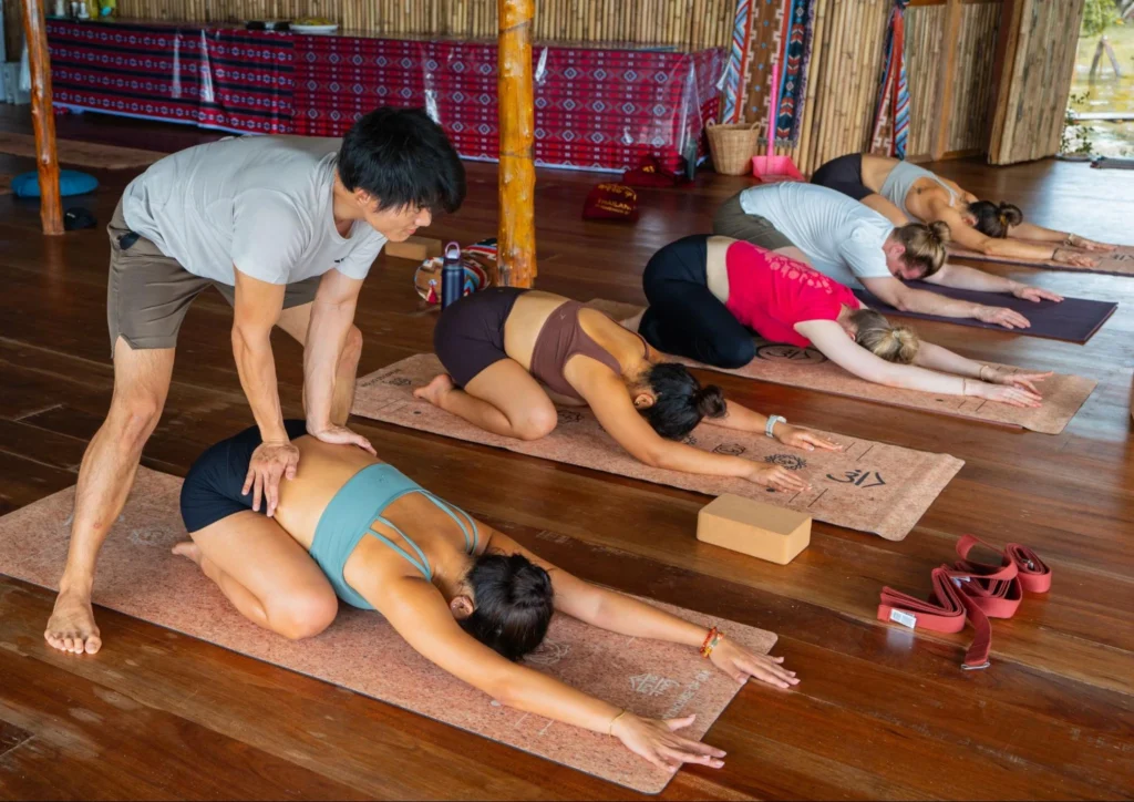 Yoga teacher assisting a student in child pose during yoga teacher training in Thailand