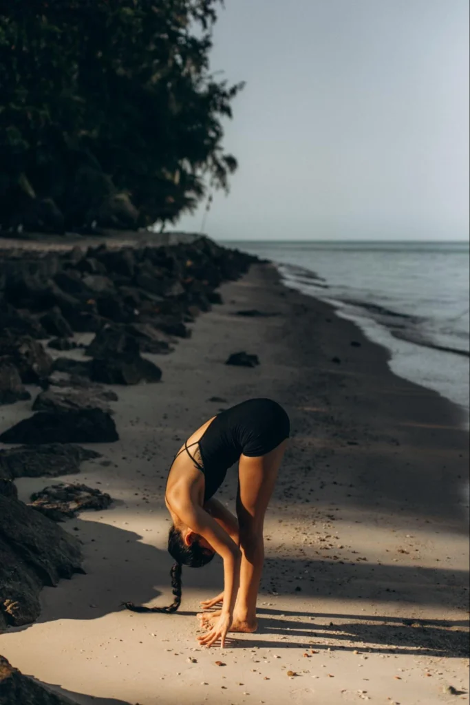 Woman practicing a standing forward fold on a quiet tropical beach in Thailand