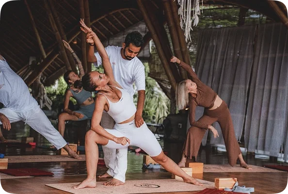 Yoga teacher assisting a student with alignment during a standing pose practice