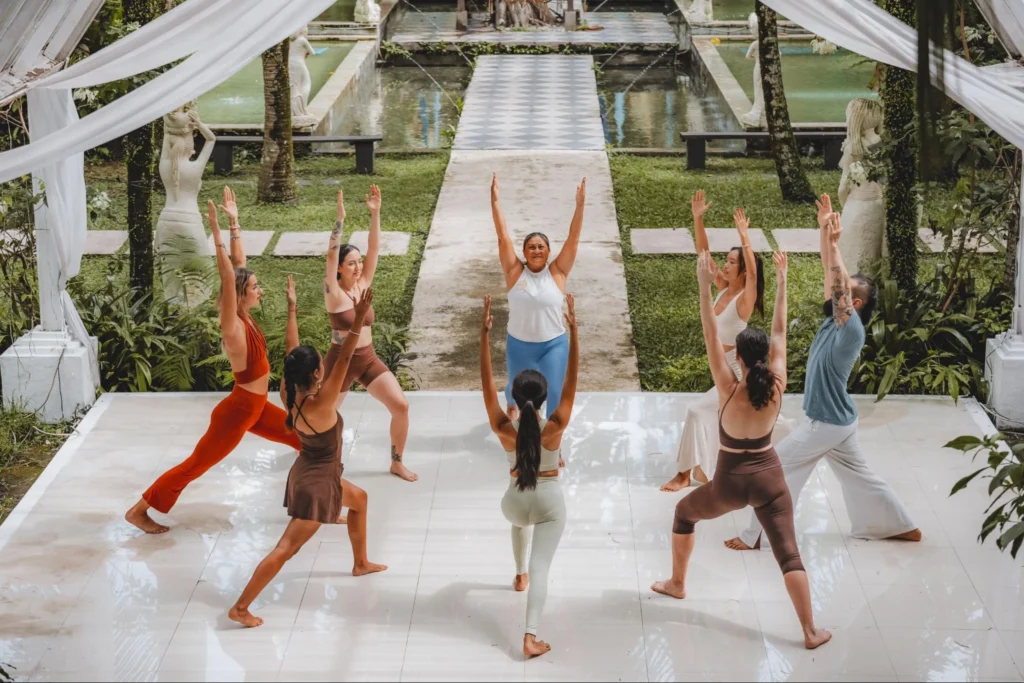 Students practicing standing yoga poses with arms raised during beginner yoga teacher training