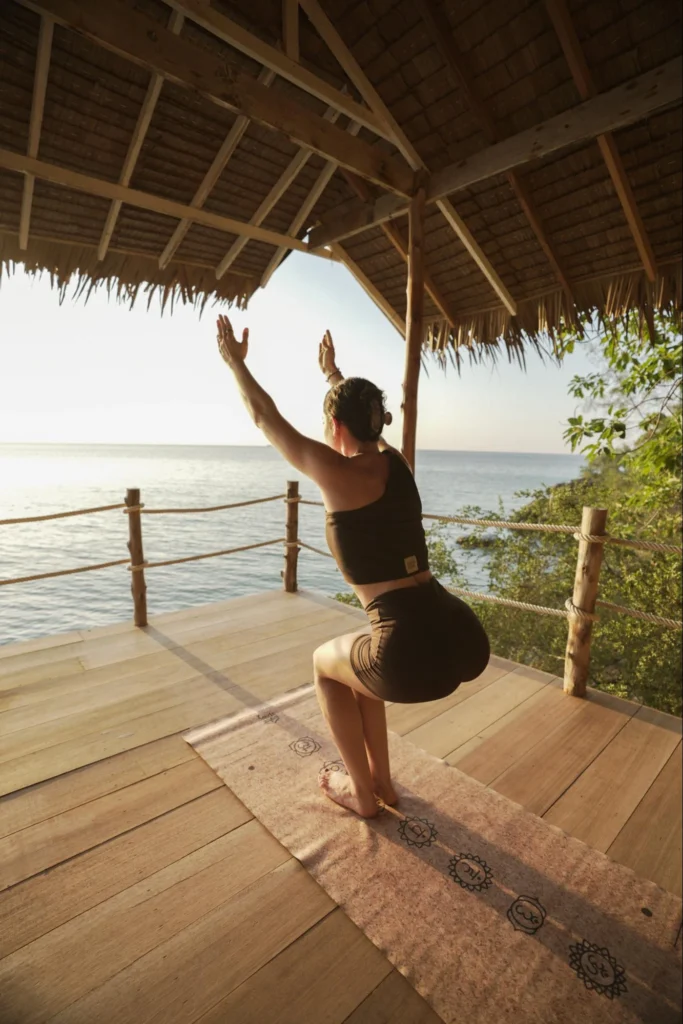 Woman practicing Chair Pose on an open-air yoga deck overlooking the ocean
