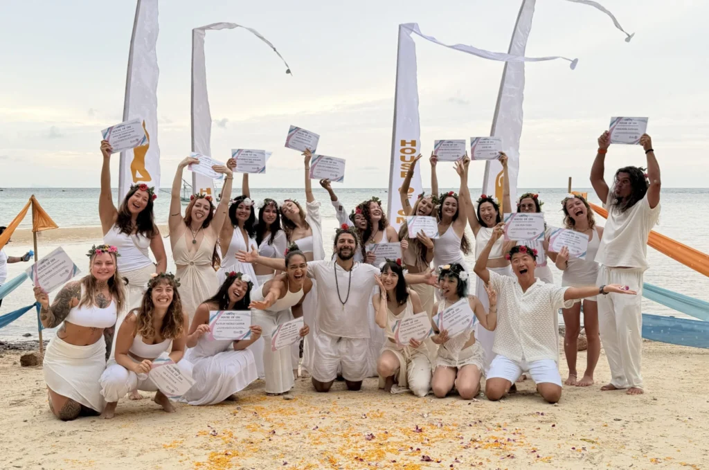 House of Om yoga teacher training graduates celebrating with certificates on the beach