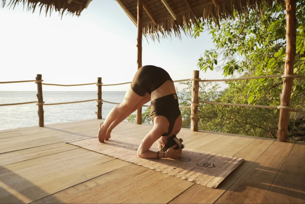 Woman practicing a supported yoga inversion on an open-air seaside deck