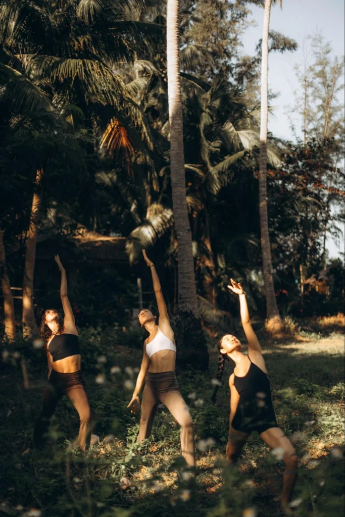 Three women practicing standing yoga poses together among tropical palm trees