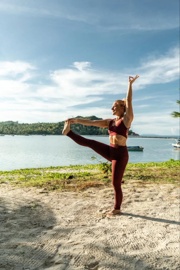 Woman practicing a standing leg extension during yoga training by the sea