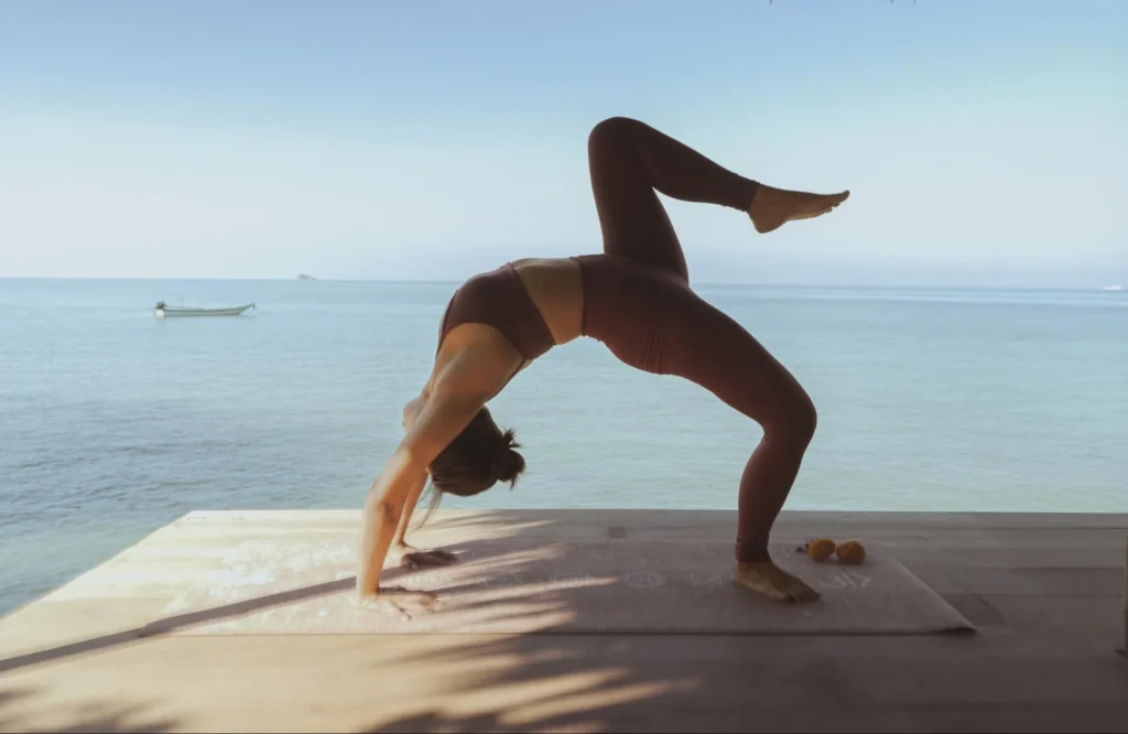 Woman practicing an advanced backbend in an open-air seaside yoga studio