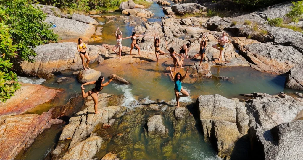 Yoga teacher training students practicing yoga on rocks beside a tropical stream in Thailand