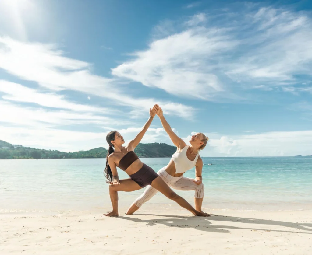 Two women practicing partner yoga on a tropical beach during Vinyasa yoga teacher training in Thailand