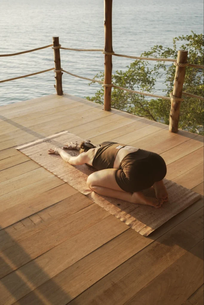 Woman resting in Child’s Pose during yoga teacher training by the sea