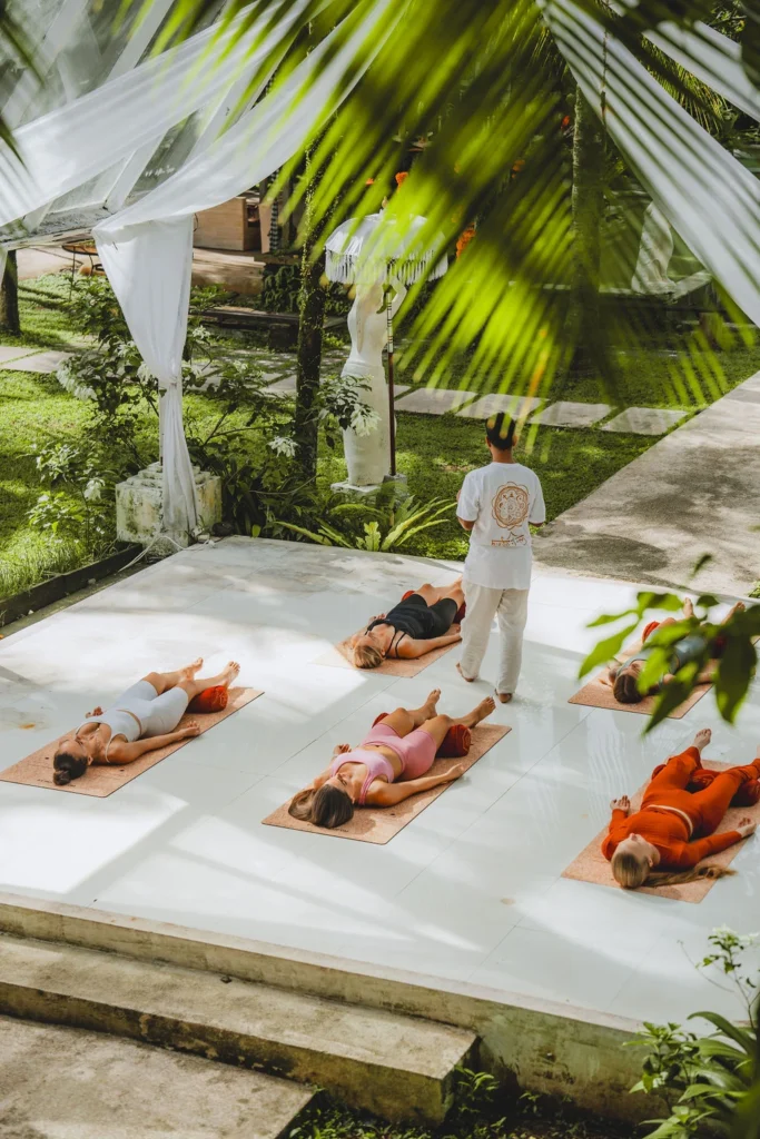 Yoga students resting in Savasana while an instructor leads a relaxation session in Bali