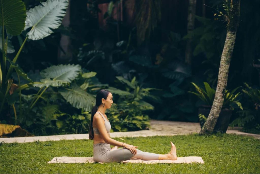 Yoga student seated on a mat practicing a mindful stretch in a tropical garden
