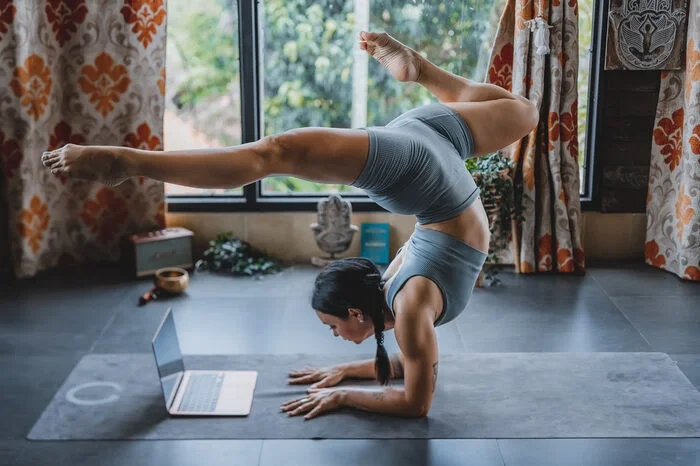Woman practicing an advanced forearm balance while following an online yoga class