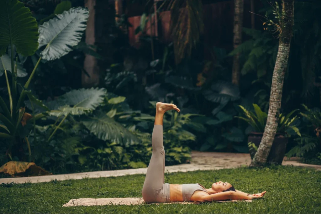 Woman practicing a leg raise yoga exercise outdoors in a lush tropical garden