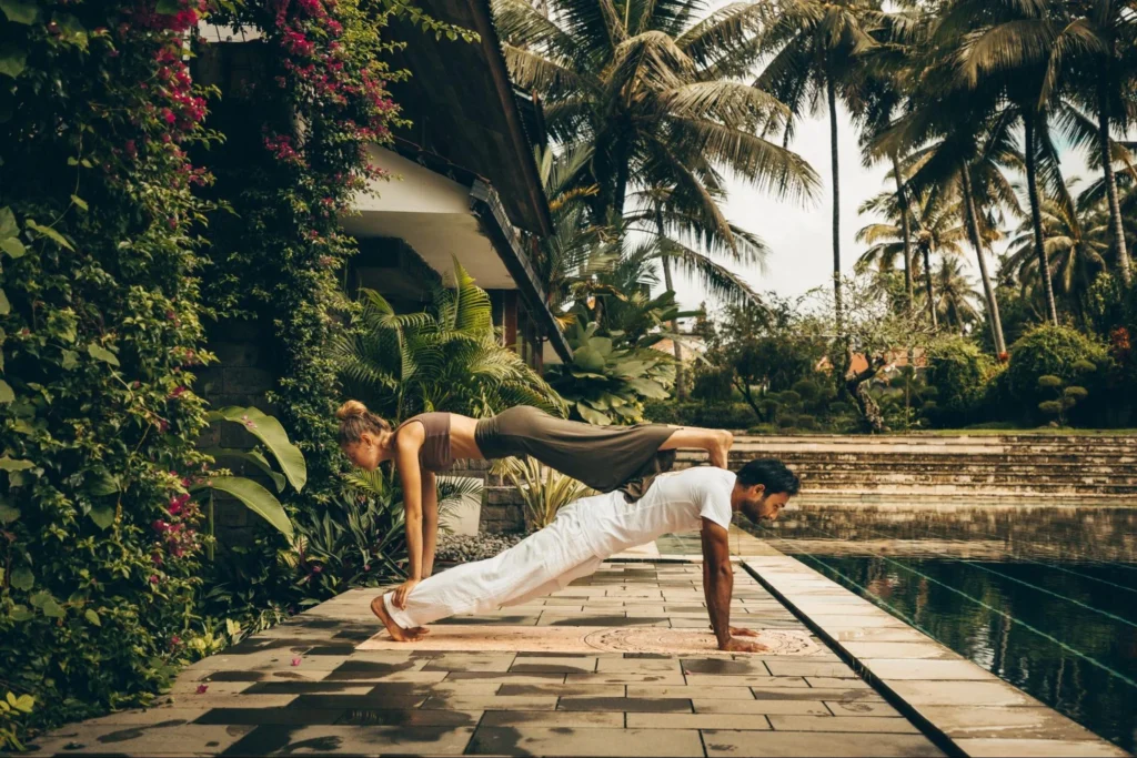 Yoga partners practicing a strength and balance pose beside a tropical pool during yoga teacher training in Bali