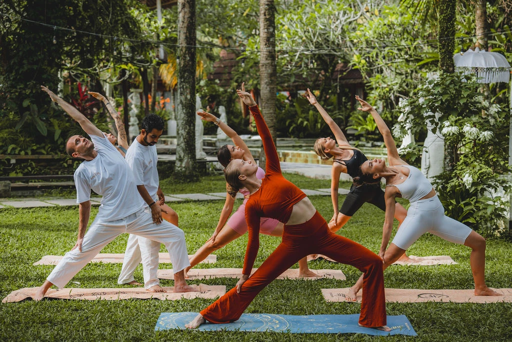 Students practicing Triangle Pose during an outdoor yoga teacher training class at The Mansion in Bali