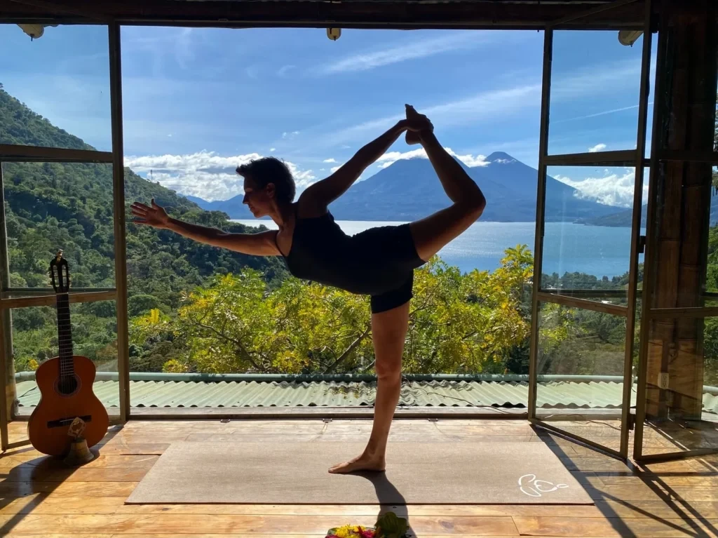 Yoga practitioner holding Dancer Pose in a studio overlooking mountains and a lake