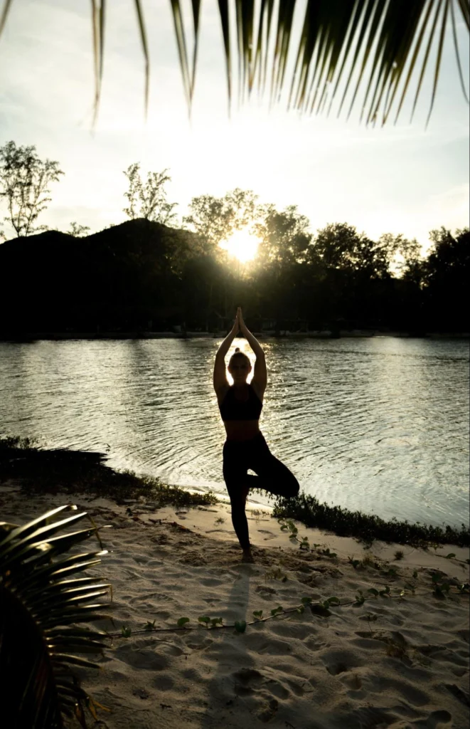 Woman practicing Tree Pose at sunset beside the sea in Thailand