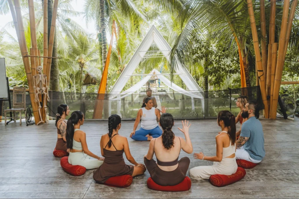 Yoga teacher training group practicing together in an open-air Bali studio