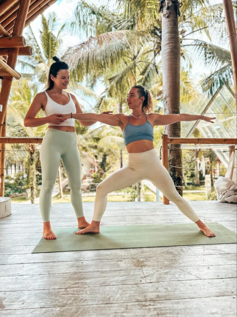 Yoga teacher assisting a student in Warrior II pose during teacher training in Bali