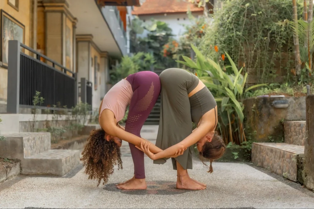 Two yoga students practicing partner forward fold during yoga teacher training in Bali