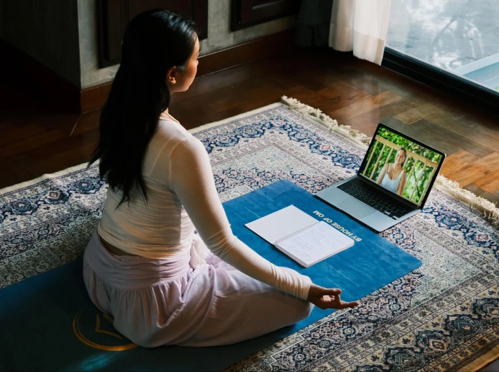 Student meditating while attending online yoga teacher training on a laptop