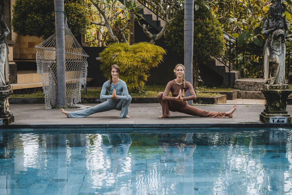 Yoga students practicing seated side stretches beside a swimming pool during yoga teacher training in Bali