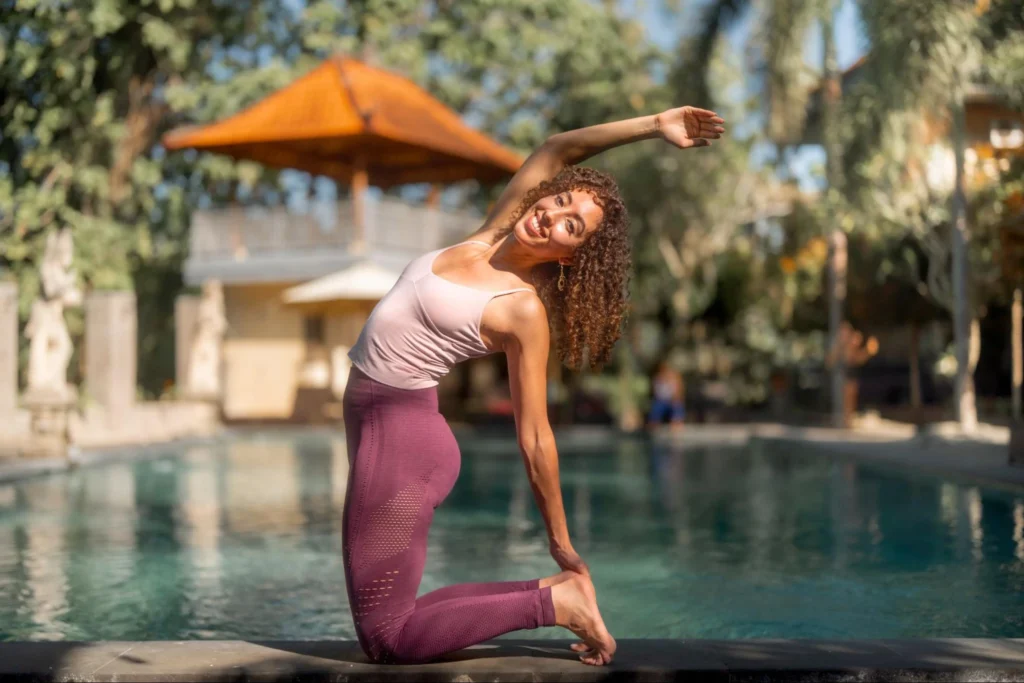 Yoga student practicing a kneeling side stretch beside the pool at Amertham in Bali